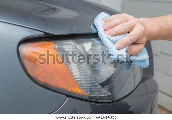 Man\'s hand with rag cleaning a dirty car lamp in\
the garage. Early spring washing or regular wash up. Professional\
car wash by hands.
