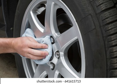 Man's Hand With Rag Cleaning A Dusty Car Wheel Disk In The Garage. Early Spring Washing Or Regular Wash Up. Professional Car Wash By Hands.