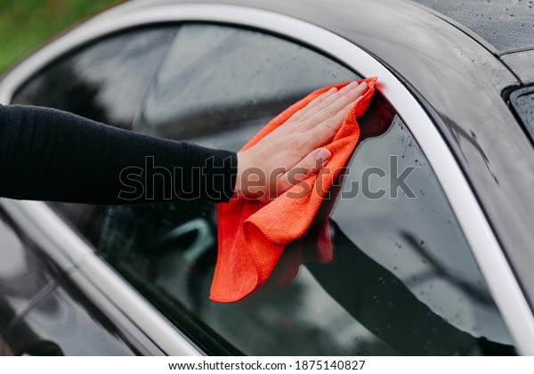Mans hand with rag cleaning side window of black\
car. Professional auto wash concept. Regular wash up. Wiping water\
droplets on vehicle