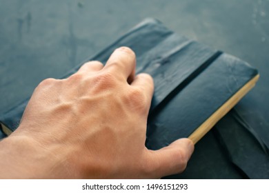 Man's hand reaching out to grab a weather worn leather journal.