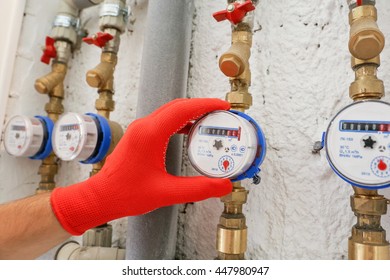 Man's Hand In A Red Glove, Brass Pipes, Valves And Water Meters In The House. To Take Readings Of Water Meters. Water Meter Installer