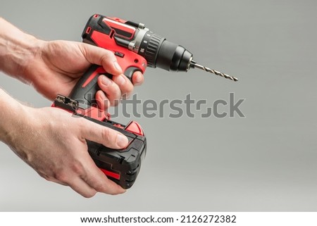 a man's hand removes the battery from a cordless tool. A man inserts a battery into a screwdriver. Repair and construction concept on gray background
