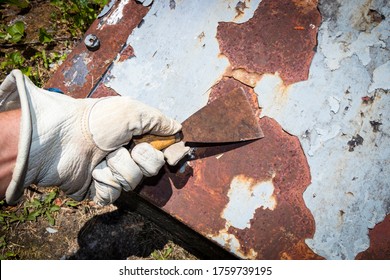 Man's hand removing paint and rust damage from metal doors using a metal paint scraper