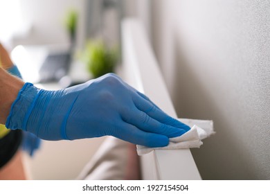 A Man's Hand In Rubber Gloves Wipes The Dust From The Head Of The Bed With A Napkin. Disinfection At Home, Cleaning In The Context Of The Covid-19 Pandemic.