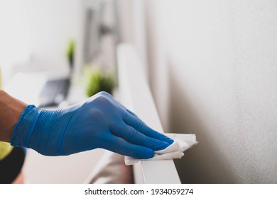 A Man's Hand In Rubber Gloves Wipes The Dust From The Head Of The Bed With A Napkin. Disinfection At Home, Cleaning In The Context Of The Covid-19 Pandemic.