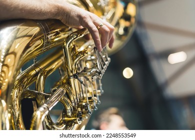 A man's hand is seen playing a large brass instrument tuba as part of an orchestra during a ceremony. Face not shown. Concept of music, performance, or celebration.