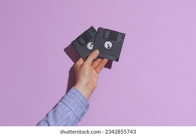 Man's hand in shirt holding black floppy disks on purple pastel background with shadow