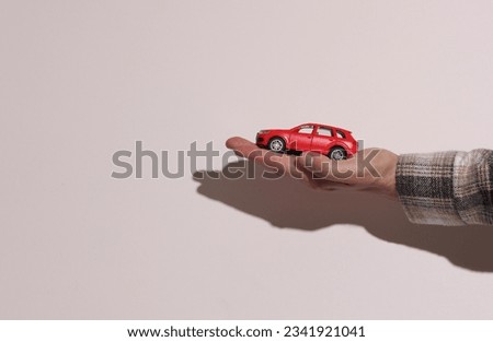 Man's hand in shirt holding toy car on beige background with shadow