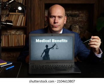 Man's Hand Showing Laptop With Phrase Medical Benefits - Closeup Shot On Grey Background
