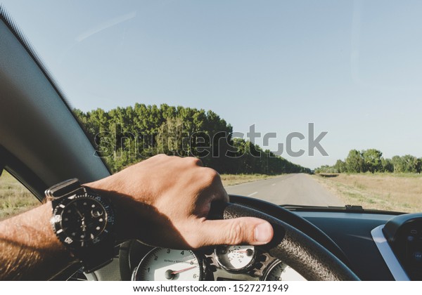 a man\'s hand with with a\
smart watch on steering the wheel of a car while driving down the\
highway. A man is driving on the road outside the city. inside\
view