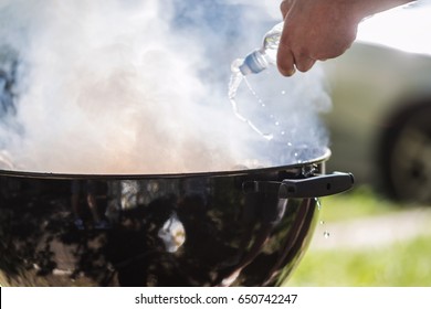 Mans Hand Spraying Water From The Bottle On The Grill.