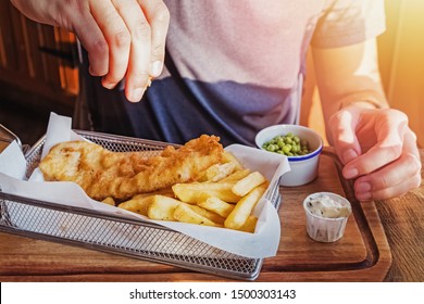Man's hand sprinkling with lemon fresh delicious portion of fish and chips close-up