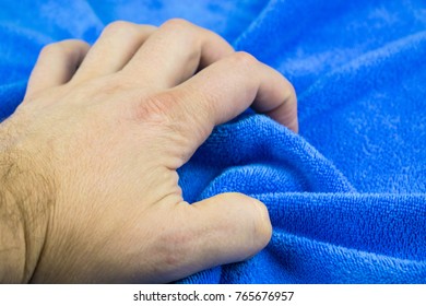 A man's hand squeezes blue fabric.