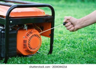 Man's hand starts a gasoline electric generator standing on the grass pulling the rope starter in summer day