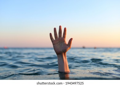 A Man's Hand Sticking Out Of The Water In The Sea At Sunset. A Drowning Man Giving A Signal With His Hand.Concept: Danger On The Water.Selective Focus