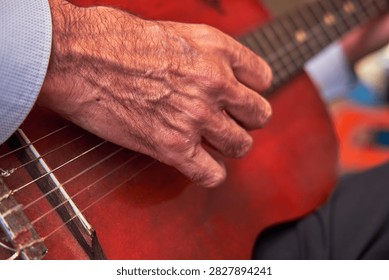 Man's hand strumming nylon strings on a red acoustic guitar during a performance