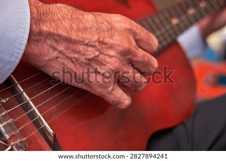 Man's hand strumming nylon strings on a red acoustic guitar during a performance