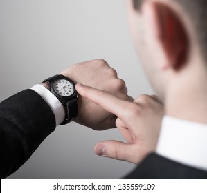 Man's Hand In The Suit Pointing On His Watch On A Gray Background