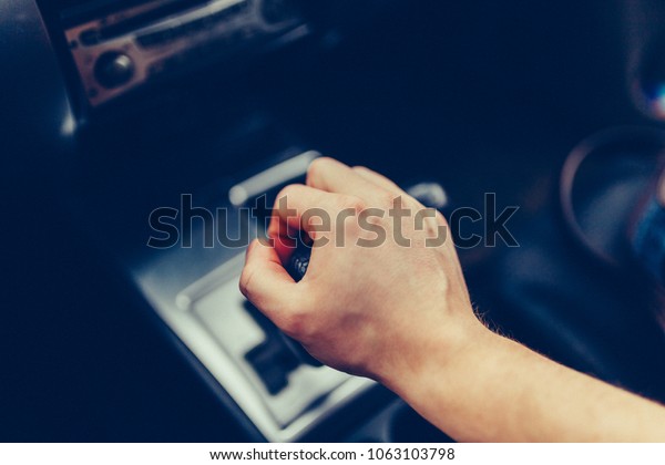 Man's hand switches automatic transmission
closeup. Close up view of gear lever manual transmission car
interior parts. Stylish Toned Photohand shifting an automatic car,
luxury car design
interior