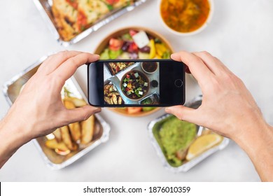 A Man's Hand Take A Shoot On Phone, Vegetarian Photography. Application Food Blogger Critique, Restaurant Delivery Concept. Italian Cuisine: Salad, Focaccia, Business Lunch. Top View, Light Background