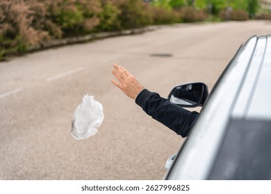 A man's hand throwing garbage from the window of his car into the road and polluting the environment.