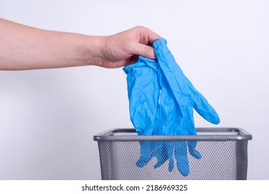 A Man's Hand Throws Blue Medical Gloves Into A Trash Can Against A Gray Background. Medical Waste.