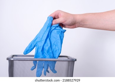 A Man's Hand Throws Blue Medical Gloves Into A Trash Can Against A Gray Background. Medical Waste.