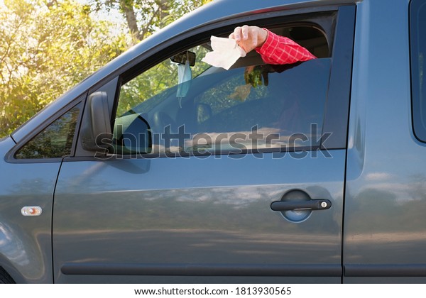 Mans hand throws trash from the car window on the\
road. Side view