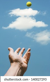 Man's Hand Tossing Tennis Ball Against A Blue Sky