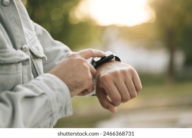 Man's hand touching a smartwatch. Smart watch on a man's hand outdoor. Close up shot of male's hand uses of wearable smart watch at outdoor in sunset. Smart watch.