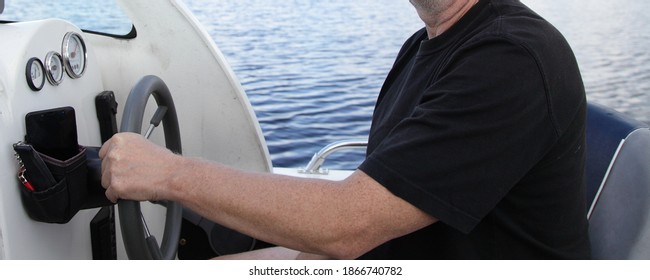 Man's hand in t-shirt holding floating motor boat steering wheel, cabin watercraft interior dashboard with control devices at summer day on water background, outdoor boating active travel recreation