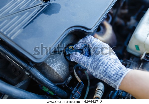 Man\'s\
hand unscrews the cap of the oil filler neck of the engine.\
Mechanic gloves change engine oil, service\
engine.