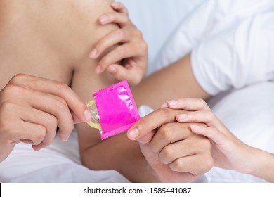 The man's hand was unwrapping the condom and the woman's hand touched his arm on the white bed. - Powered by Shutterstock