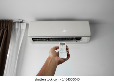 Die Hand des Menschen mit einem Fernbediener. Hand, die rc hält und die Temperatur der Klimaanlage auf einer weißen Wand anbringt. Temperatur des Innenraumkomforts. Gesundheitskonzepte und Energieeinsparungen.