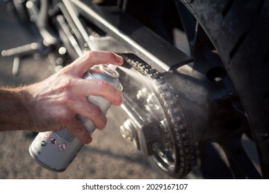 Man's hand using spray can to clean and protect motorbike chain. Concept of maintenance and lubrication of the motorcycle chain.