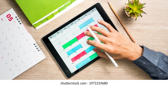 Man's hand using tablet computer to create business planning on calendar. Flat lay and top view of working space
