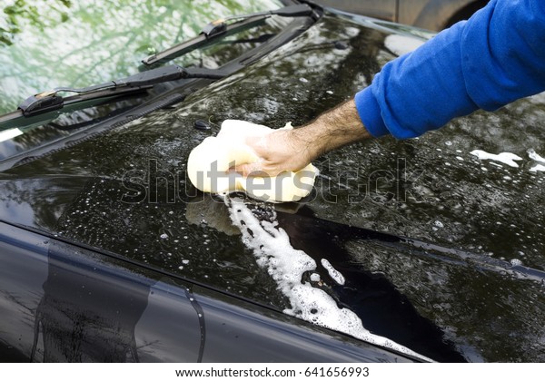 The man\'s hand washes the car\'s sponge mask with\
plenty of foam.