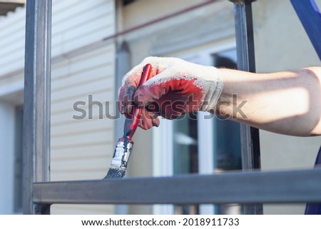 a man's hand in a white and red glove paints a metal structure with a brush.