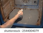 A man`s hand wiping surface in greasy oven. Paper towel gets dirt on it. Kitchen and oven cleaning