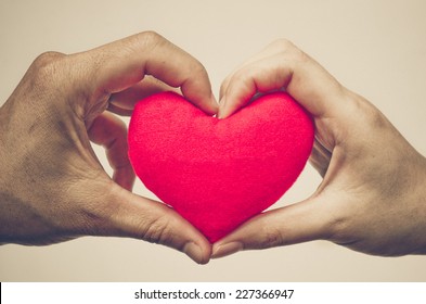 man's hand and woman's hand holding a red heart