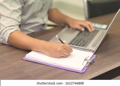A man's hand is writing something on a white notebook and a laptop that looks to the side.Office workers writing text on white paper with mobile phones.