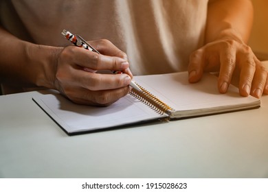 man's hand written in a spiral notepad placed on a wooden table with items.Man hand with pen writing on notebook