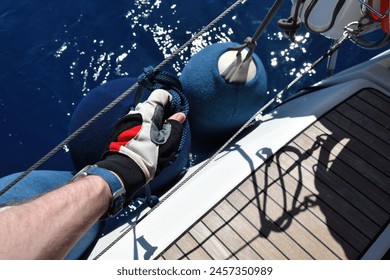 A man's hand in a yachting glove pulls rope knot of the fender attachment point - Powered by Shutterstock