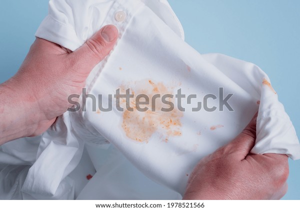 Man\'s handing hold clothes with a stain from tomato\
sauce. top view