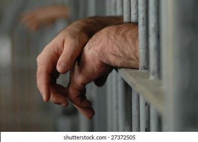 mans hands behind bars in jail or prison