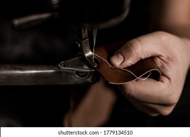 Man's hands behind old sewing machine. Professional tanner working on piece of brown leather, close up.  - Powered by Shutterstock