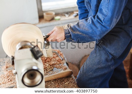 Man's hands in  blue jeans suit working with woodcarving machine and wood, shavings on table, close up.