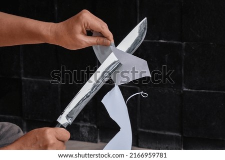 man's hands checking the sharpness of machete by cutting a piece of paper