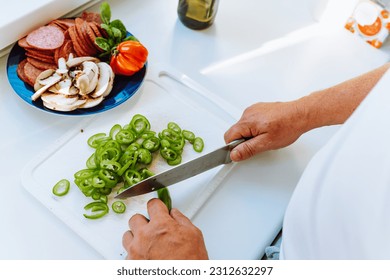 Man's hands cut peppers with knife on cutting board, slicing ingredients for pizza or salad - Powered by Shutterstock