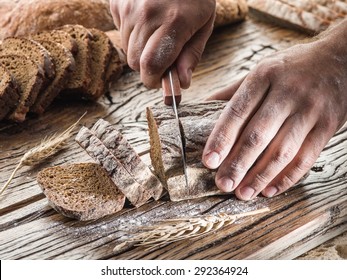 Die Hände des Menschen schneiden Brot auf dem Holzpflaster.